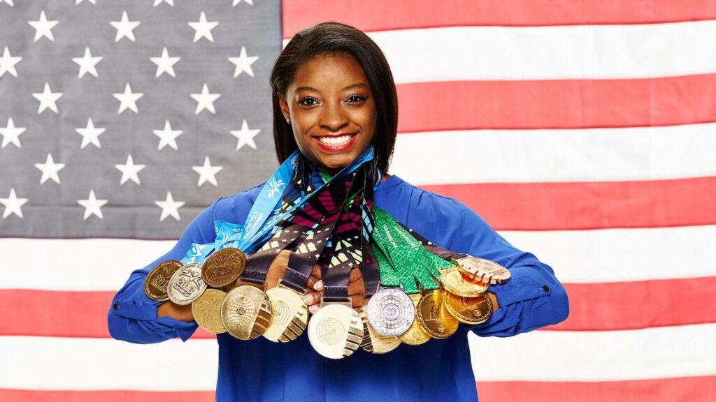 Simone Biles Medals Display Against American Flag Wallpaper