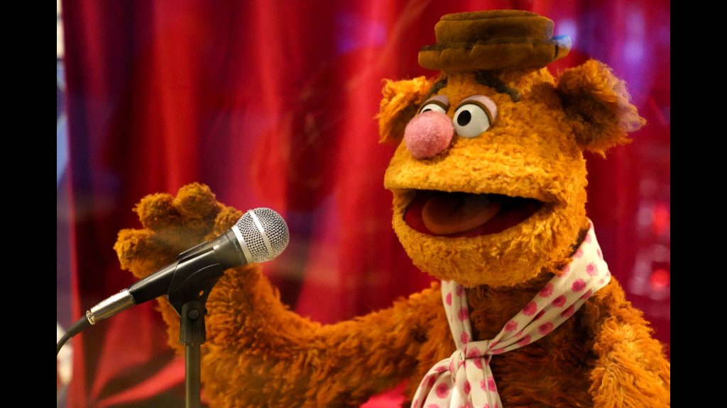 Singing Fozzie Bear with hat and neckerchief on red curtain stage wallpaper background