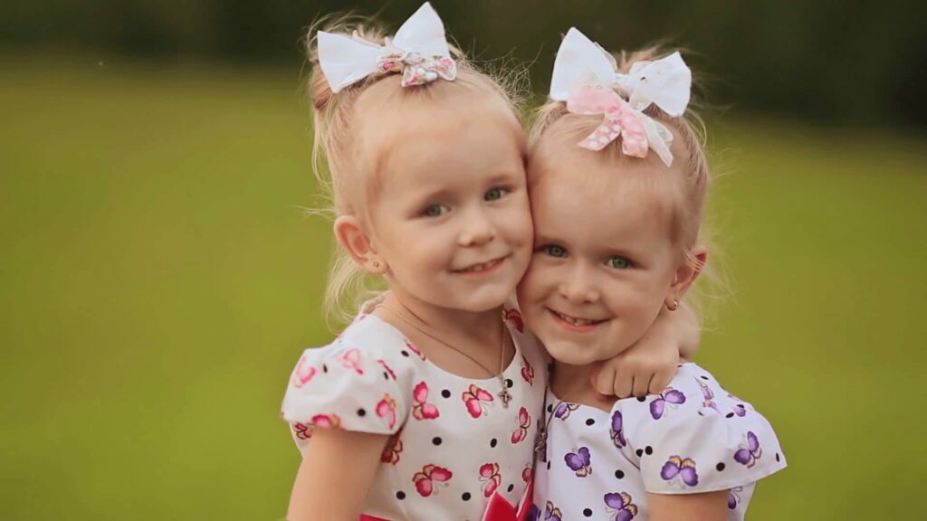 Joyful Twin Bond: Sisters' Summer Delight on Vibrant Meadow - HD Wallpaper