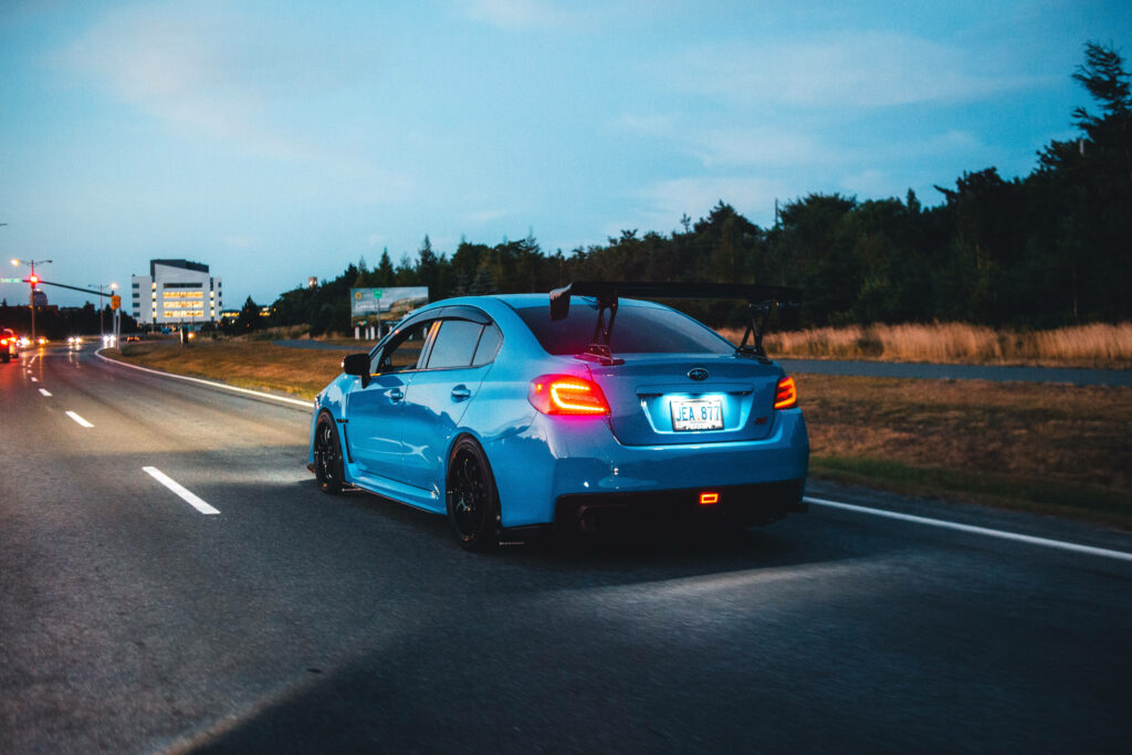Sky blue Subaru WRX STI speeding on open road at dusk with sleek design and rear wing in 4K Wallpaper