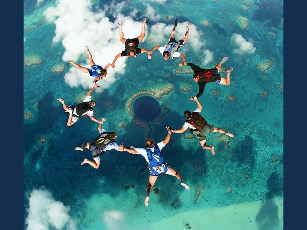 Skydivers forming circle above Belize Great Blue Hole vibrant turquoise coral aerial wallpaper