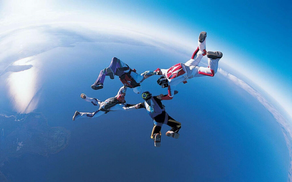 Thrilling Aerial Adventure: Daring Men Skydiving over Azure Ocean Wallpaper