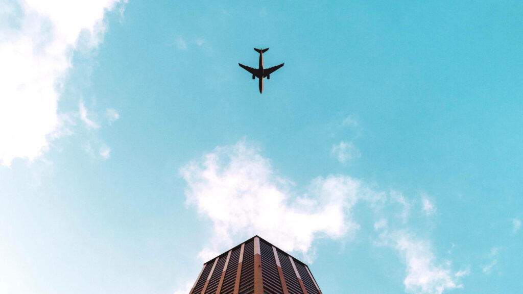 Flying High: Majestic Plane Soaring Above Rustic Architectural Charm Wallpaper