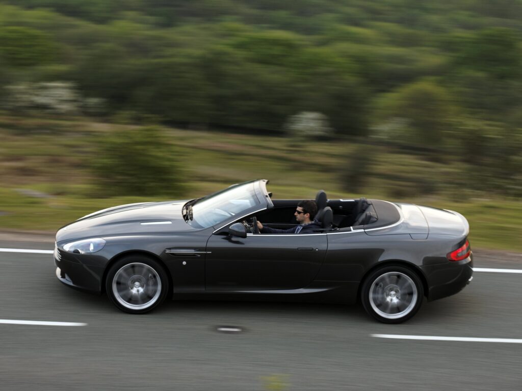 Elegant 2010 Aston Martin DB9 Driving Through Lush Greenery Wallpaper