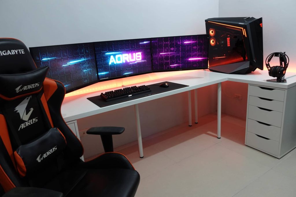 Sleek Aorus gaming room with triple monitors illuminated PC and ergonomic chair on white desk Wallpaper