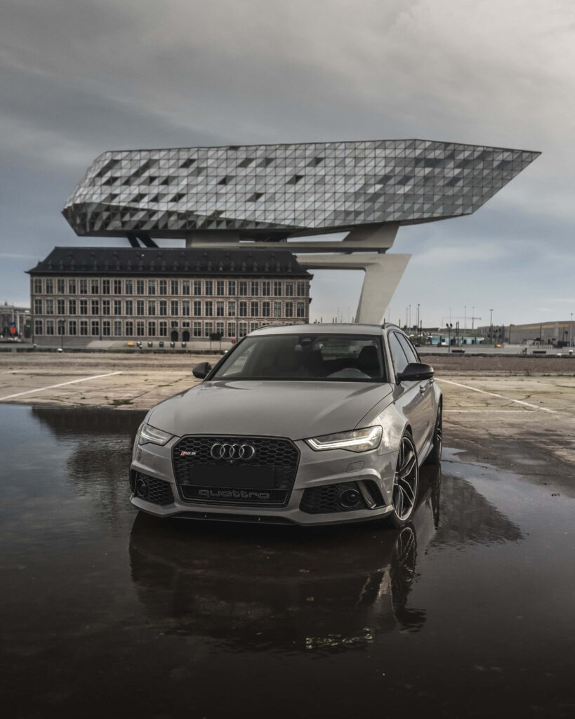 Audi sports car on wet reflective surface with modern building and overcast sky background Wallpaper