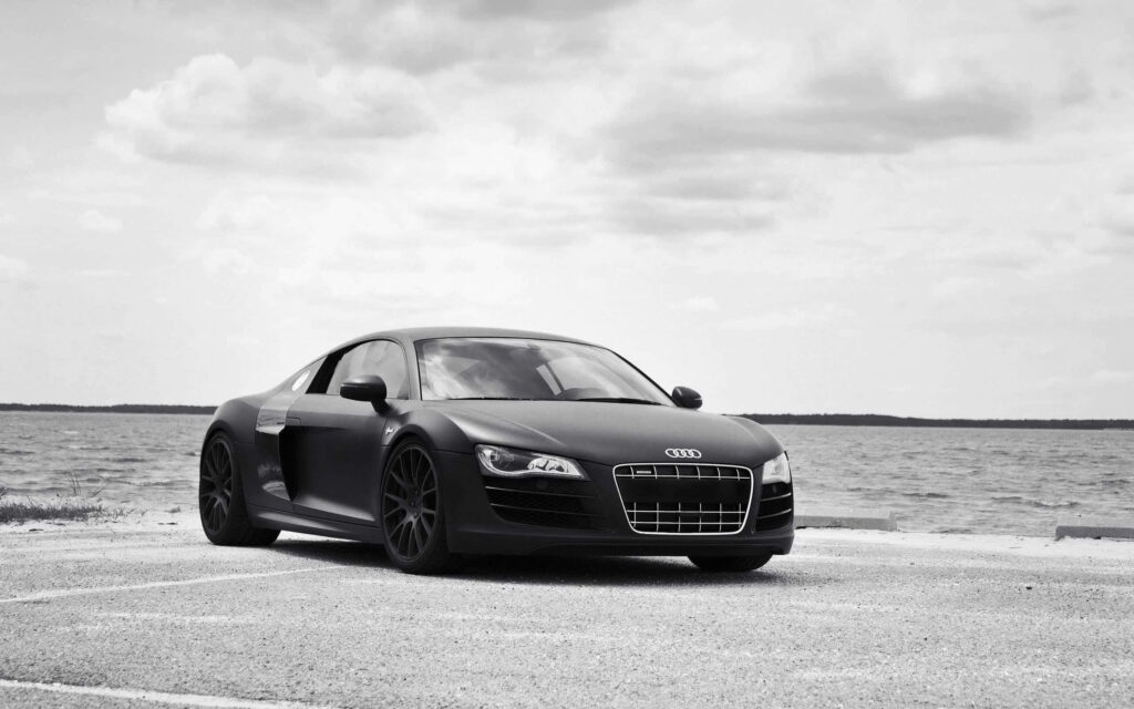 Black Audi R8 parked by seaside with calm waters and cloudy sky stylish automotive wallpaper