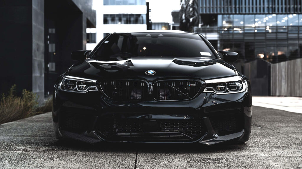Front view of sleek black BMW M5 with urban architecture reflected on glossy finish perfect wallpaper