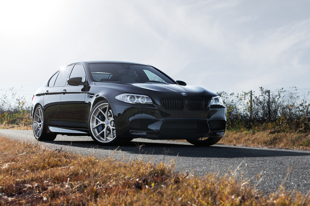 Sleek Black BMW M5 Wallpaper: Front View on Open Road with Blue Sky