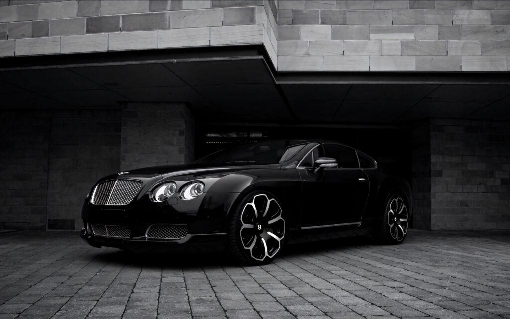 Black Bentley with flower-shaped rims parked by modern stone building luxury car wallpaper background