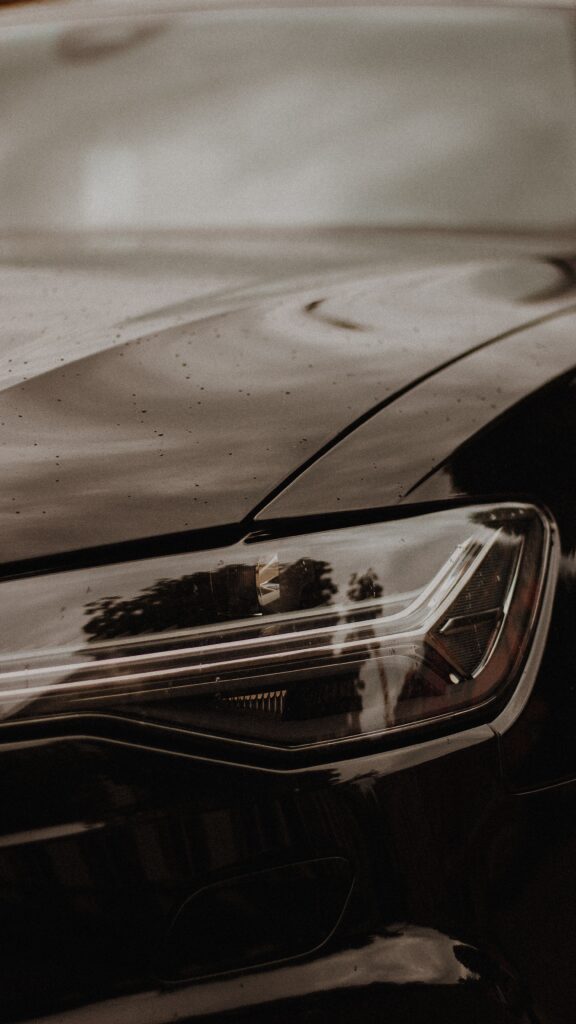 Close-Up of Sleek Black Car Headlight with Raindrops Reflection Wallpaper