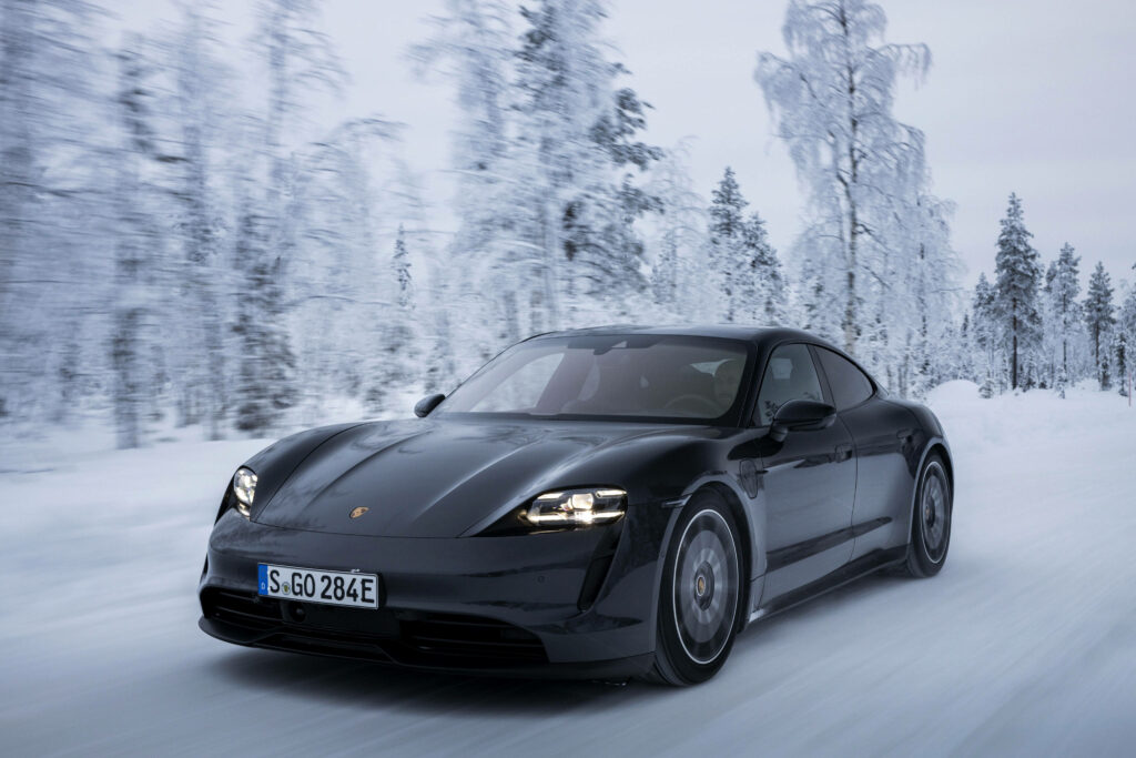 Black car speeding on snowy road with frosted trees under clear blue winter sky wallpaper background