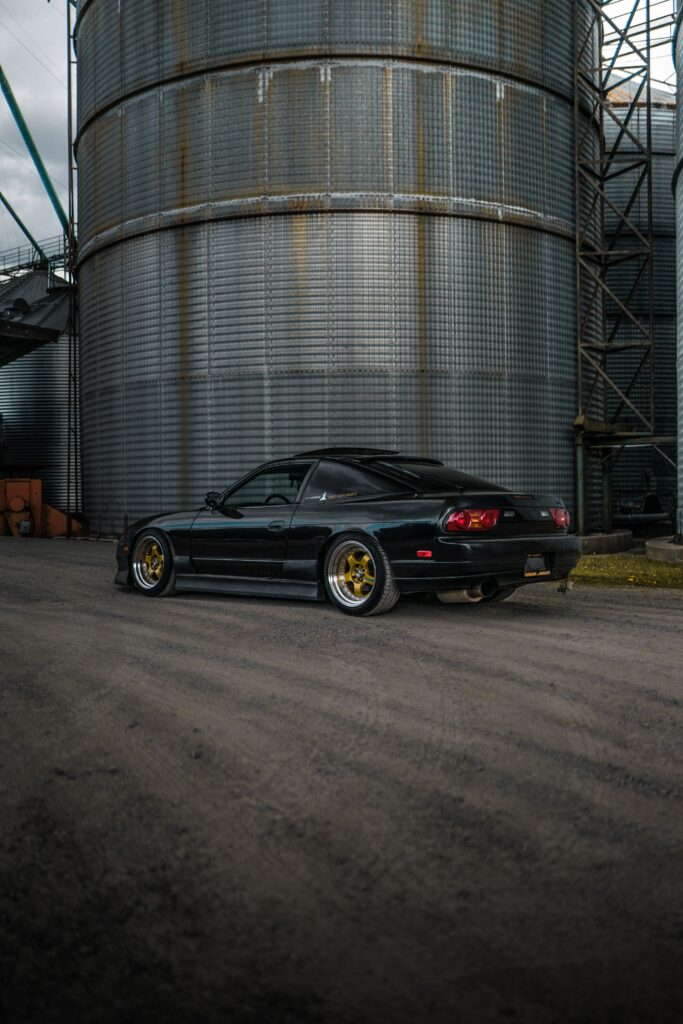 Sleek Black Car in Dramatic Side View with Industrial Backdrop Wallpaper
