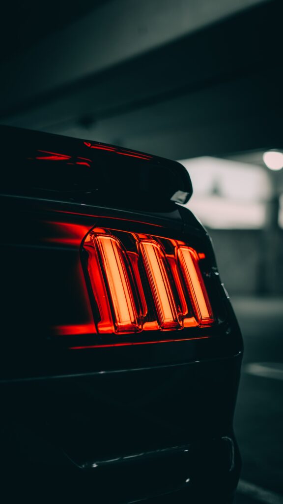 Sleek Black Car with Red Taillights in Dimly Lit Setting Wallpaper