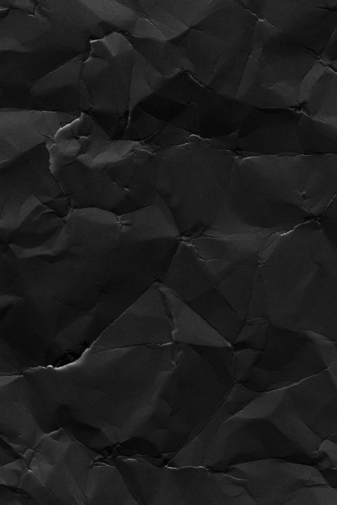 Black crumpled paper wallpaper with sharp creases dramatic lighting and deep shadows texture