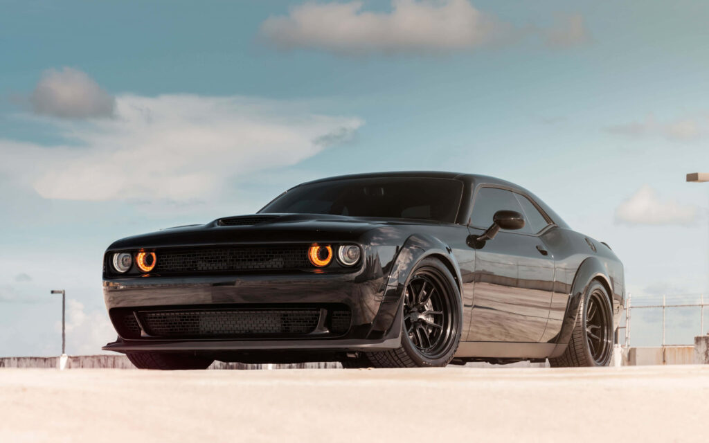 Sleek black Dodge Challenger parked under bright sky with dramatic lighting in 4K wallpaper
