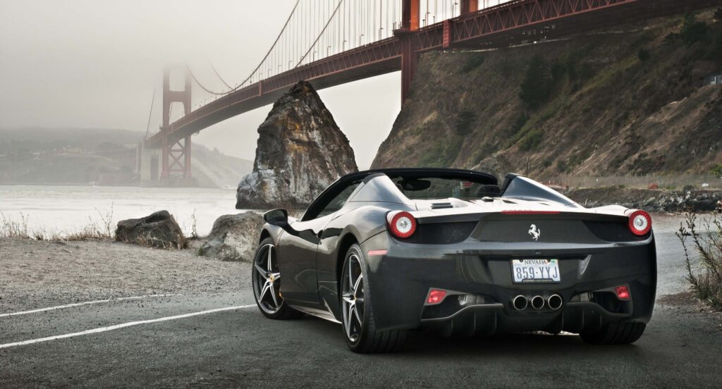 Black Ferrari parked on scenic road with misty Golden Gate Bridge in background luxury wallpaper