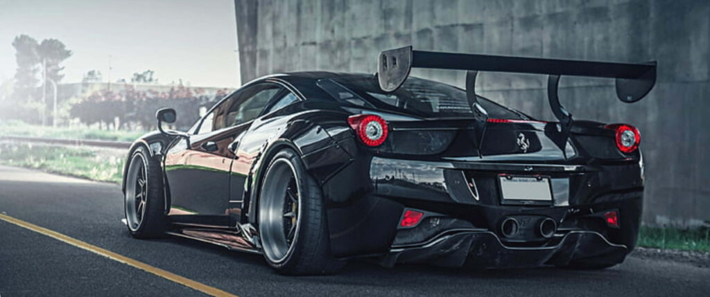 Black Ferrari with aggressive rear wing parked under urban overpass showcasing power and elegance Wallpaper