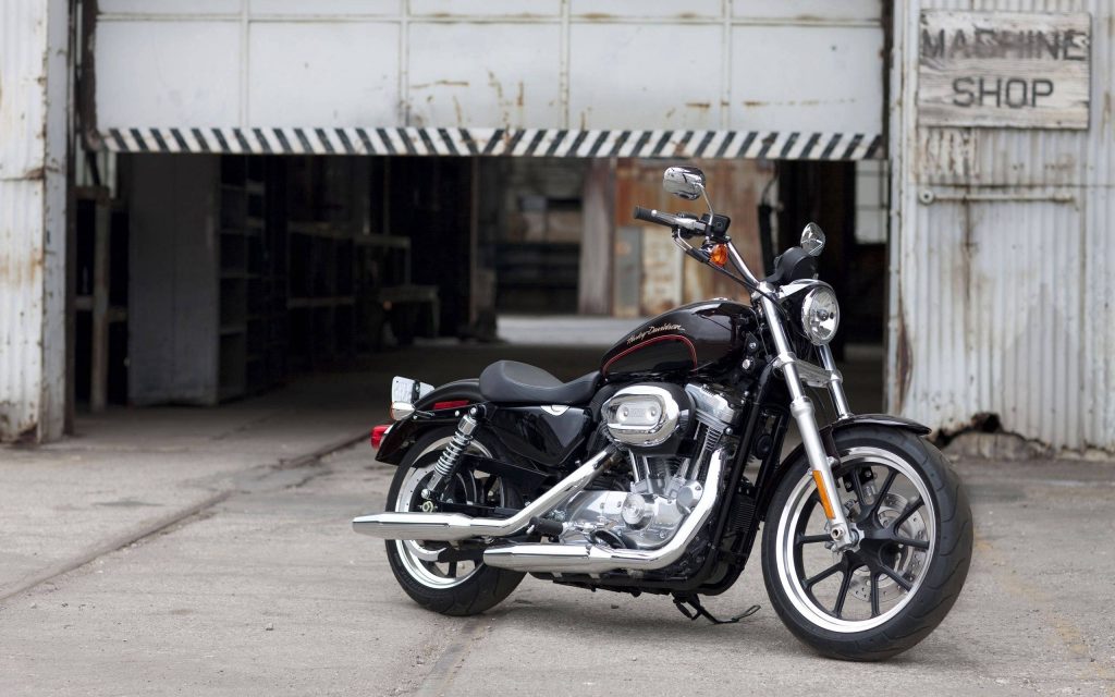 Black Harley-Davidson Sportster motorcycle with chrome accents in front of rustic Machine Shop Wallpaper