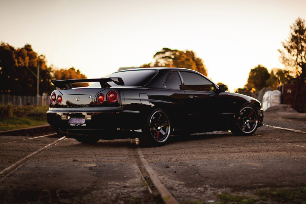 Sleek Black Nissan GT-R R34 on Railroad Track at Sunset Wallpaper