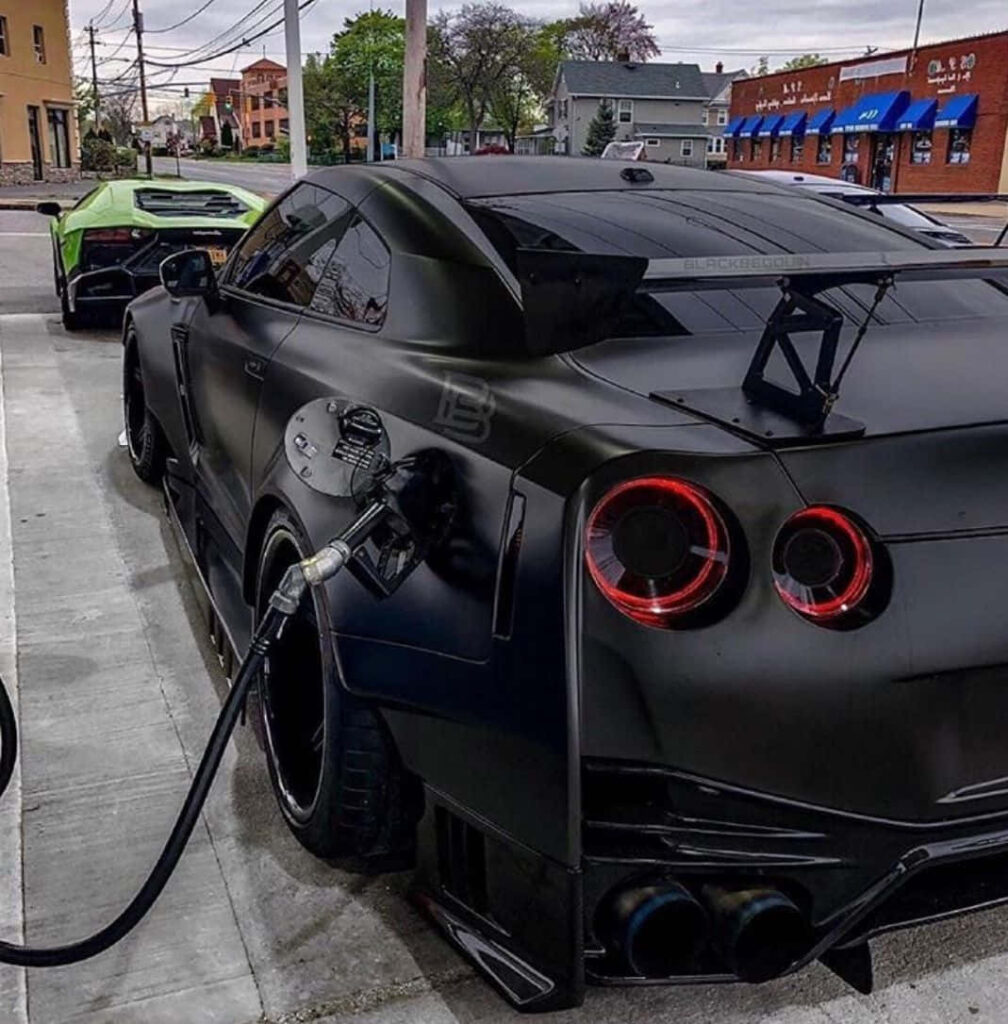 Black Nissan R35 GTR refueling at gas station with glowing taillights and bold rear wing wallpaper