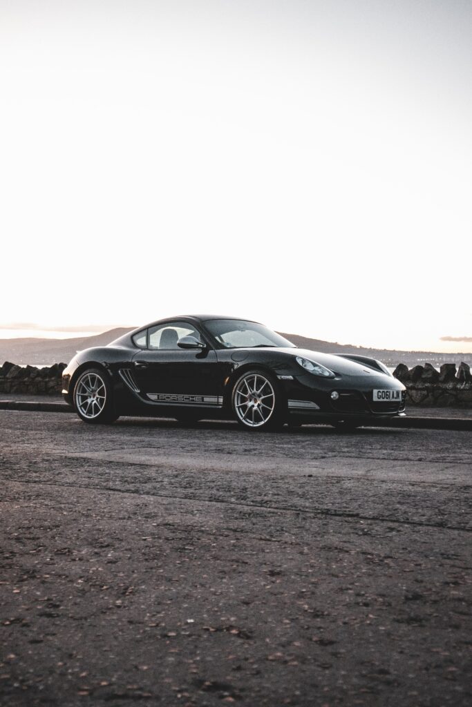Sleek Black Porsche Cayman 987 R Side View Wallpaper with Scenic Background