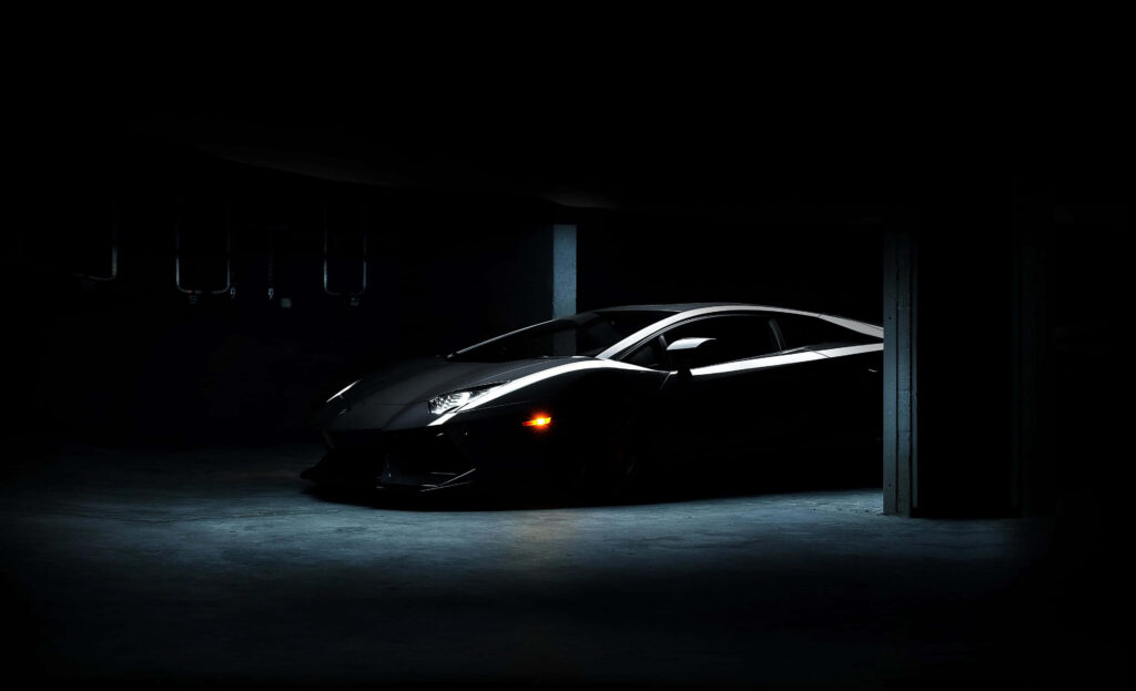 Sleek black sports car illuminated in dim garage highlighting sharp lines modern design wallpaper
