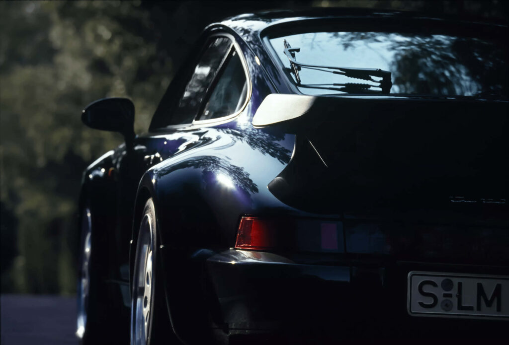 Sleek black sports car with bold rear spoiler in dramatic lighting against blurred outdoors Wallpaper