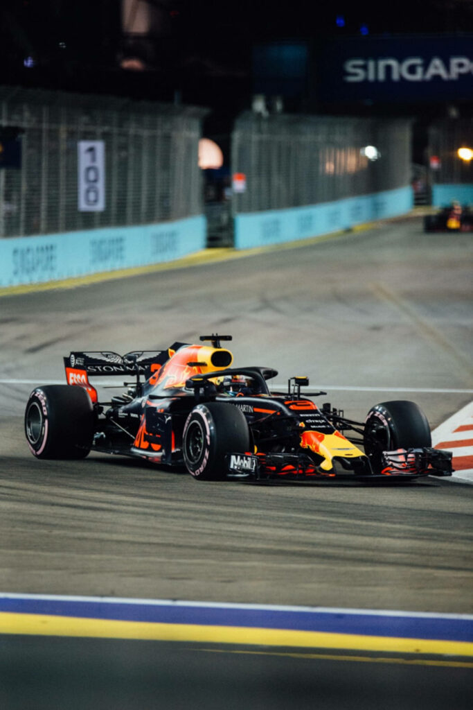 Sleek black and orange Formula 1 car racing under bright city street lights at night wallpaper