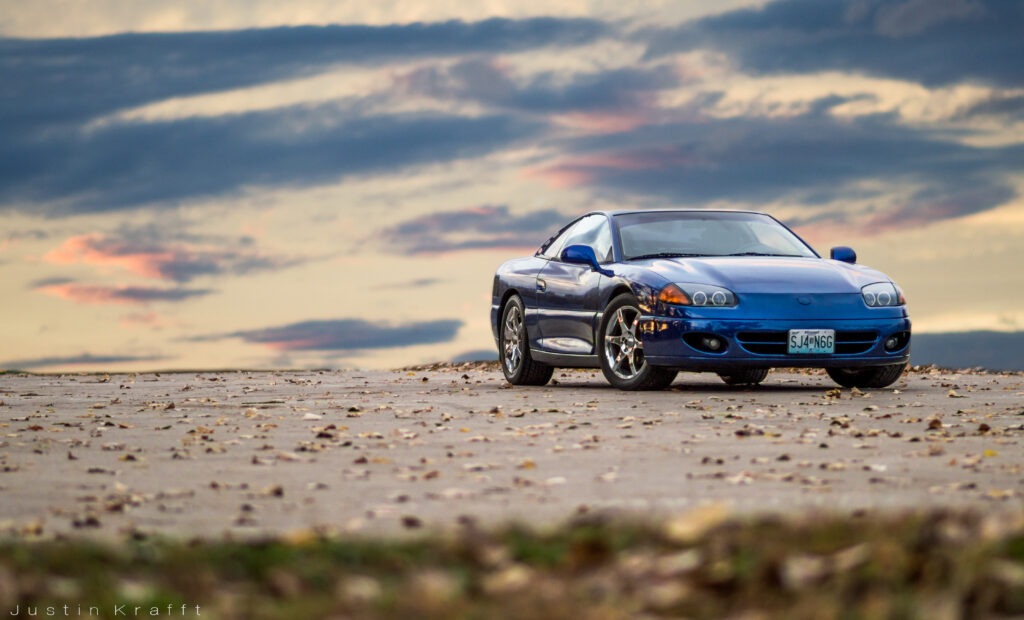 Sleek Blue Car with Headlights Against Dramatic Cloudy Sky Wallpaper