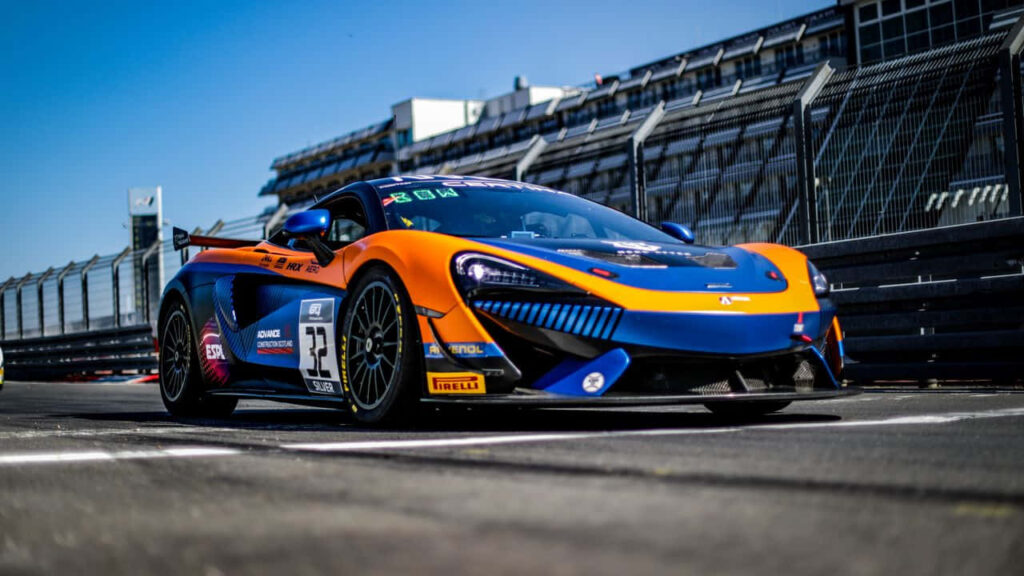 Sleek blue and orange sports racing car on sunlit racetrack with modern grandstand background Wallpaper