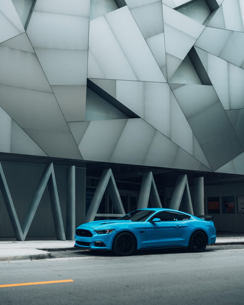 Sleek Blue Sports Car Side View on Urban Road with Geometric Building Wallpaper