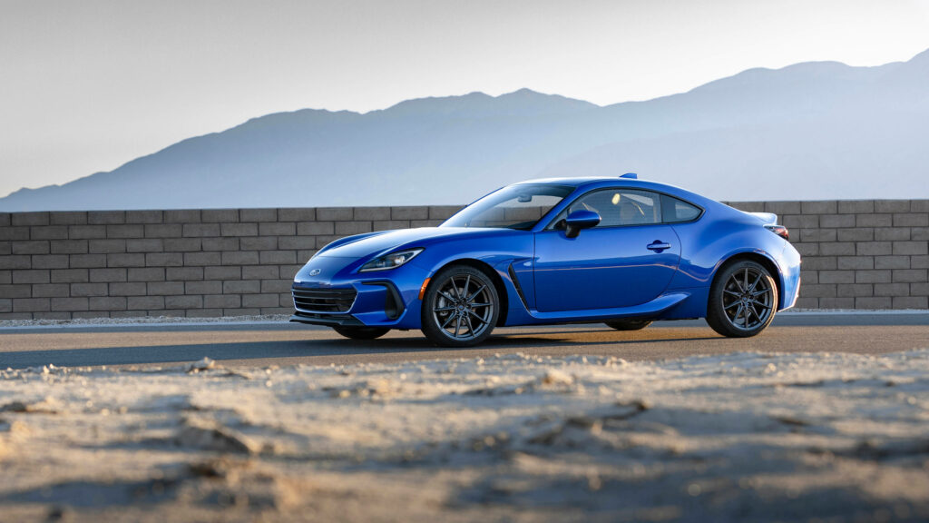 Sleek Blue Subaru BRZ Driving by Brick Wall - Mountain Wallpaper