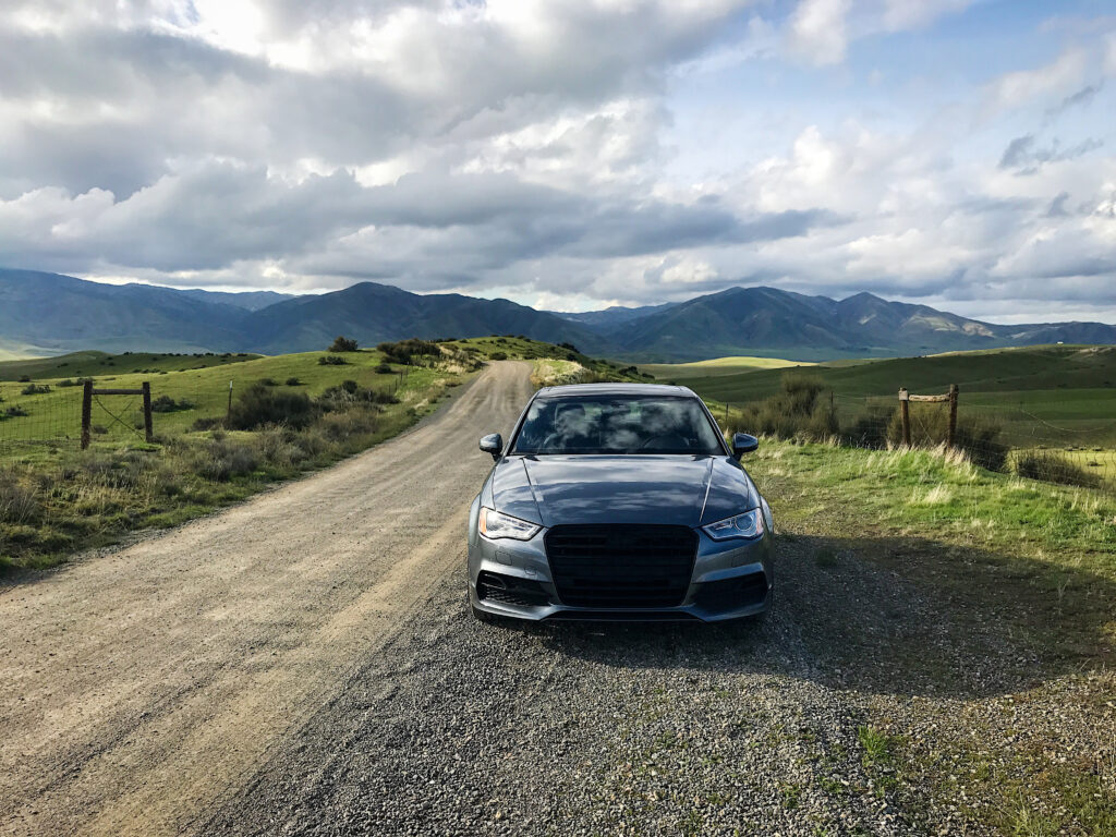 Sleek Car Wallpaper: Scenic Road & Lush Hills Under Cloudy Sky