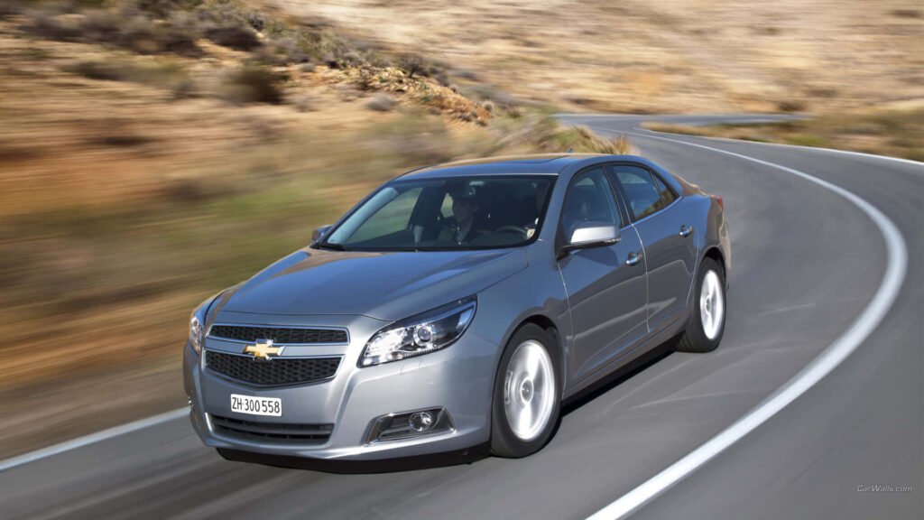 Sleek Chevy Malibu driving on winding desert road showcasing modern design and performance Wallpaper