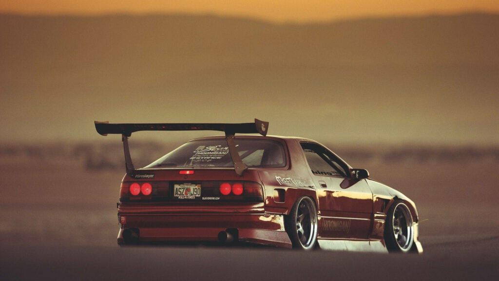 Dark red JDM performance car with aggressive rear wing parked on open road at sunset wallpaper