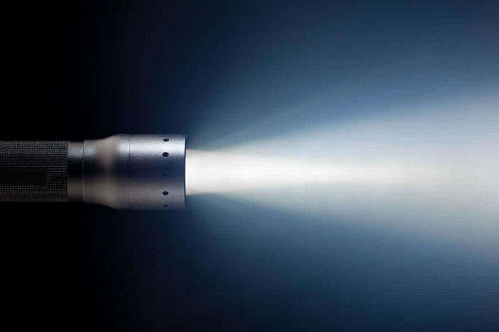 Metal flashlight shining bright white beam on deep blue gradient minimalist wallpaper background