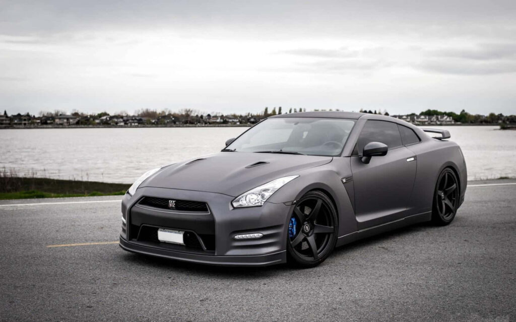 Stylish GT-R Parked by Serene Water: Elegant Matte Grey Wallpaper