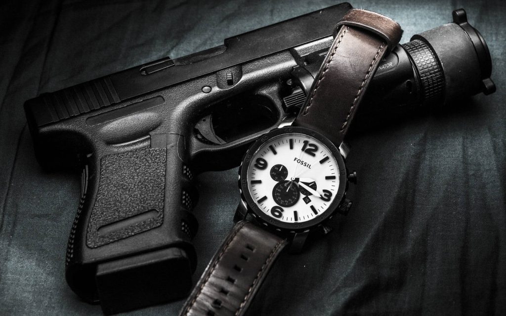 Sharp high-contrast wallpaper of sleek Glock handgun and Fossil chronograph watch on dark background