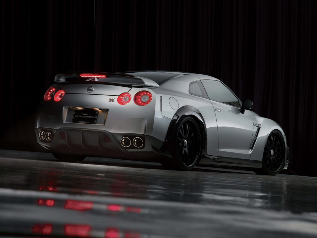 Sleek gray Nissan R35 GTR sports car rear view on reflective surface with dark curtain backdrop Wallpaper