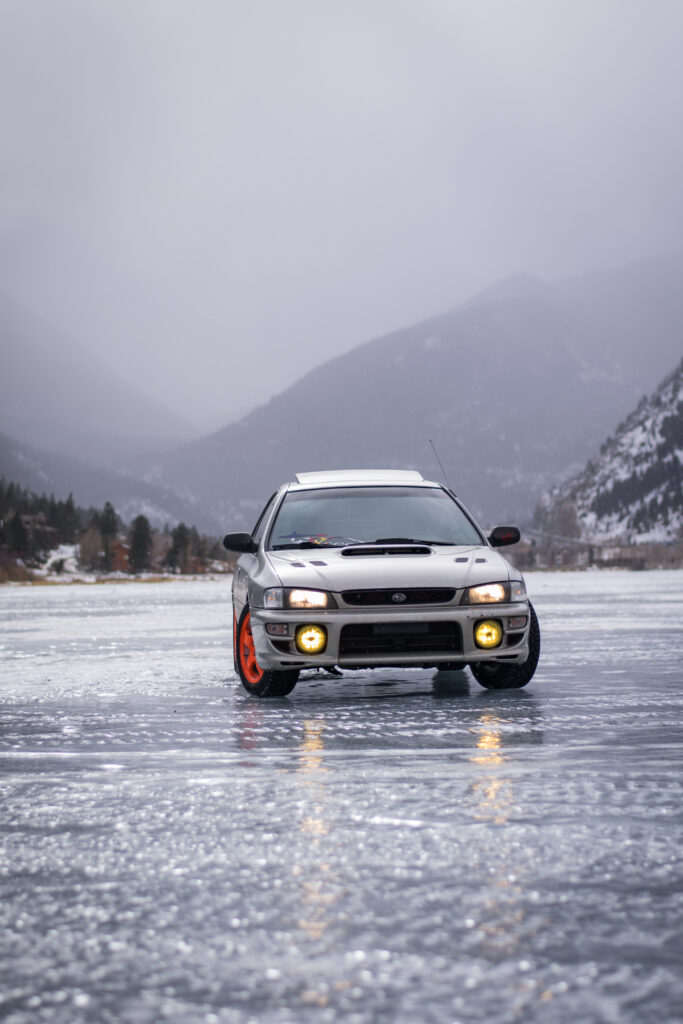 Sleek Gray Subaru on Icy Surface with Snowy Mountain Background Wallpaper