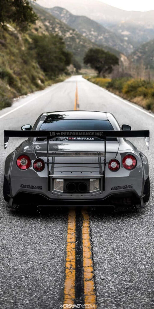 Grey Nissan R35 GTR widebody kit large rear wing parked on mountain road with double yellow lines Wallpaper