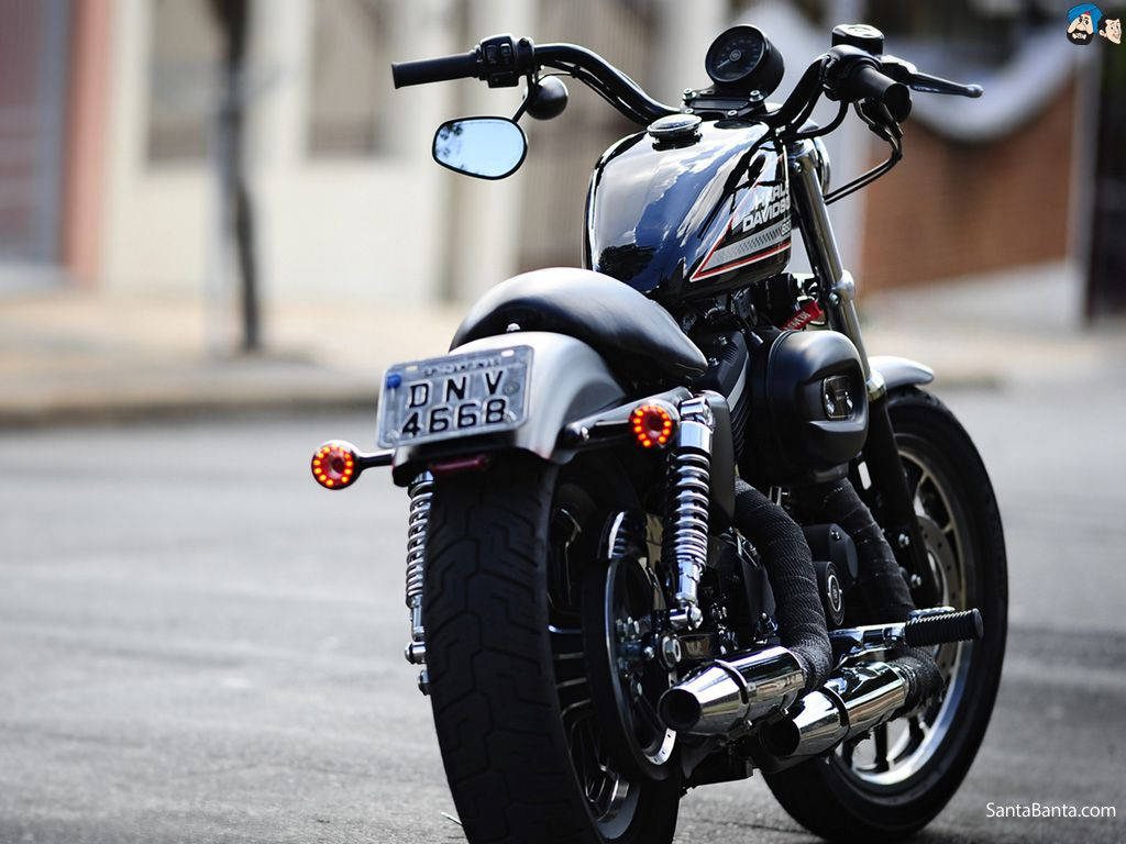 Rear view of sleek Harley Davidson motorcycle with black tank red LED signals dual exhausts urban background Wallpaper