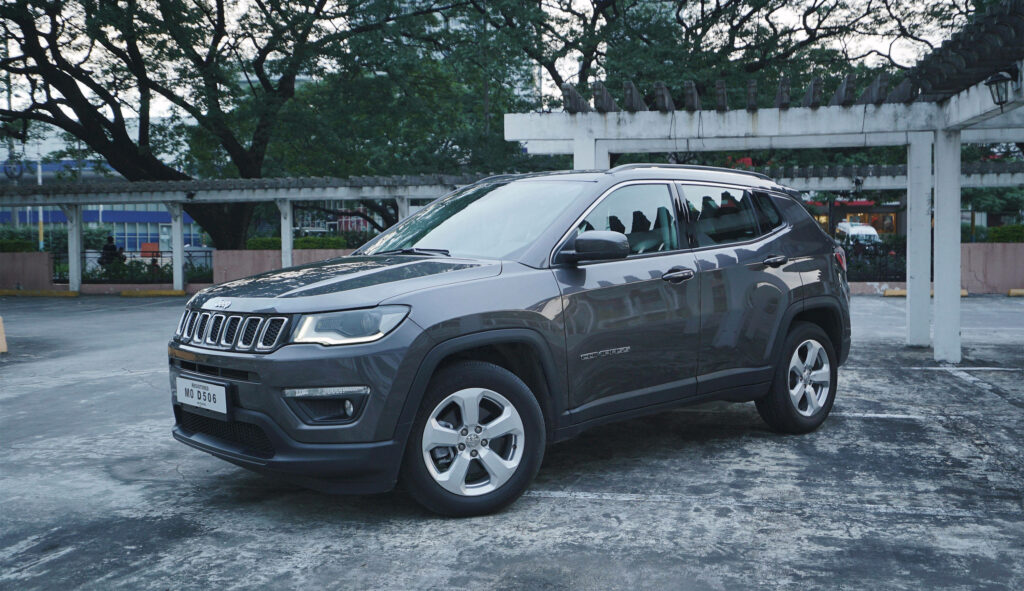 Sleek Jeep Compass parked on concrete under pergolas with trees and urban buildings background Wallpaper