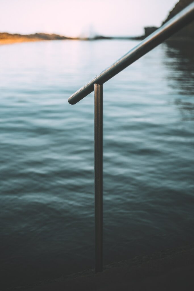 Sleek metal handrail overlooking calm lake at sunset with soft light reflecting on water wallpaper