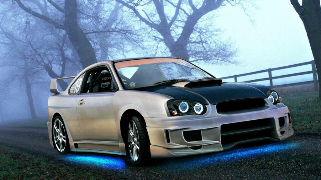 Sleek modified sports car with blue underglow on misty rural road lined with bare trees wallpaper