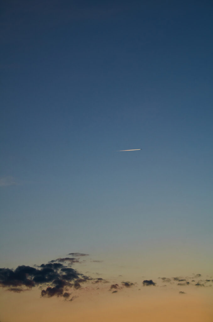 Sleek airplane flying over clouds at twilight with glowing trail and sunset to deep blue sky gradient Wallpaper
