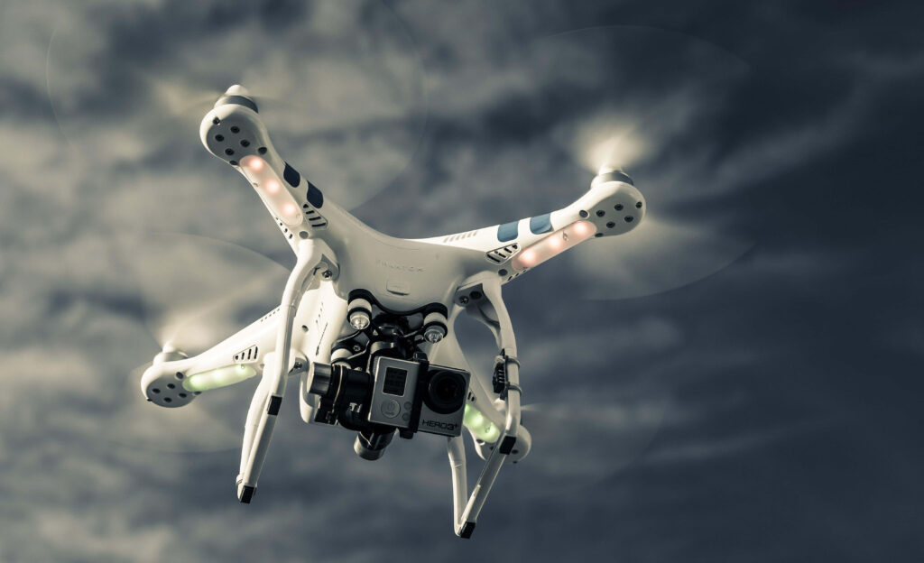 Sleek quadcopter drone with LED lights flying under dramatic cloudy sky capturing high-res footage Wallpaper