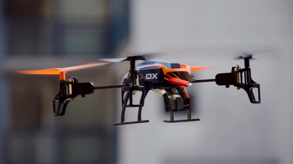 Sleek orange and black quadcopter drone hovering in urban sky showcasing modern aerial technology Wallpaper