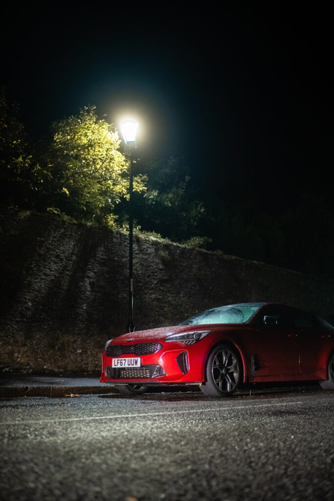 Sleek Red Car Under Lantern: Nighttime Beauty with Greenery Wallpaper